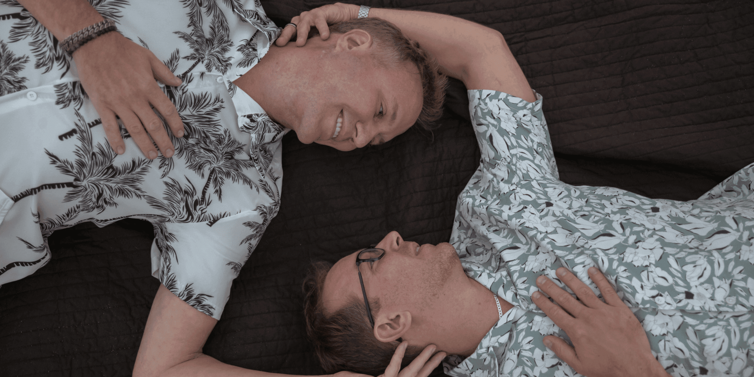 The essence of a successful match. Two men in Hawaiian shirts lie on the floor holding each other and smiling at each other after being matched by Tawkify.