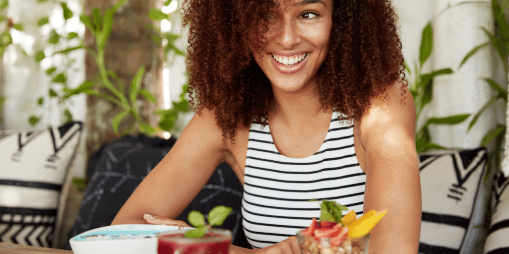 Young woman smiling celebrating single life in front of a breakfast of fresh fruit and granola.