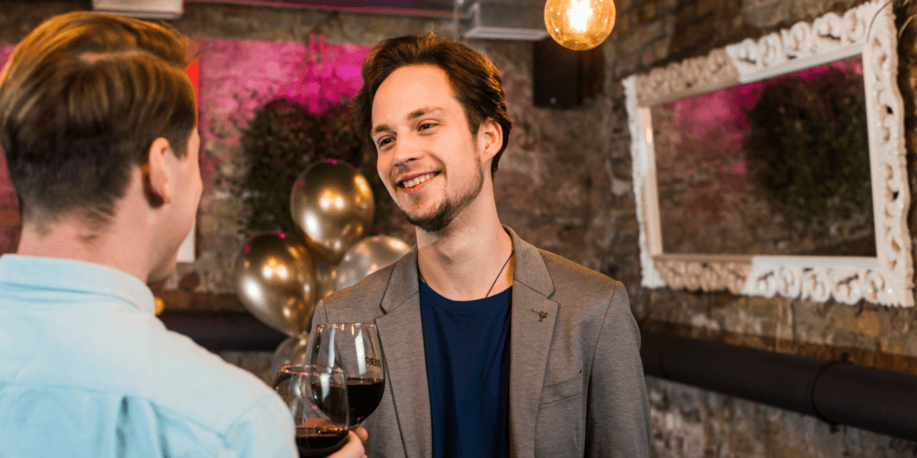 A gay male couple engage in conversation over glasses of red wine as a romantic date idea in New Jersey.