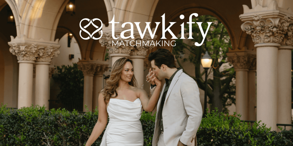 A man in a tan suit kisses the hand of a woman in a white dress on their wedding day in a courtyard after using Tawkify matchmaking services.
