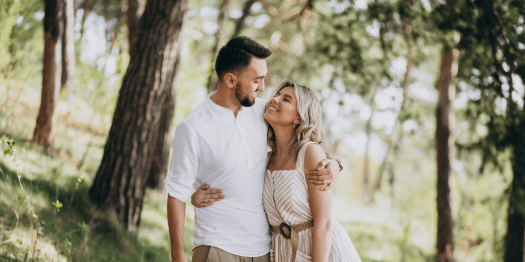 Young couple holding each tightly as they walk along a trail in a sunlit forest after being successfully matched through a matchmaking service.