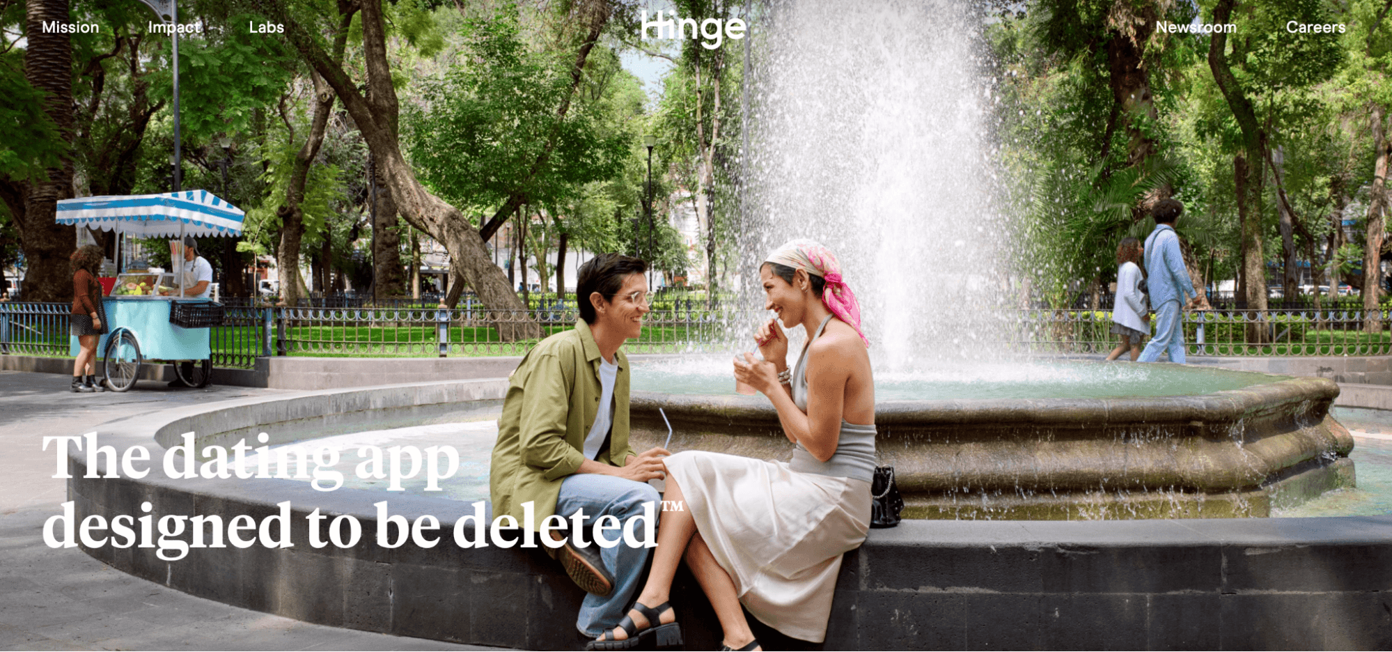 Hinge app promotional image of a couple sitting and talking beside a park fountain, with the tagline "The dating app designed to be deleted."