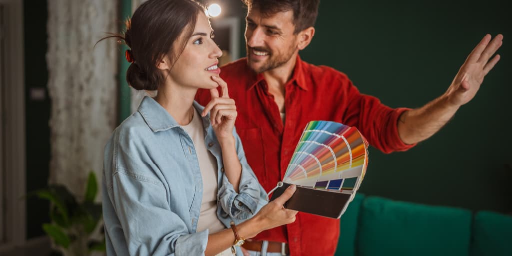A man and a woman looking at paint swatches in a living room.