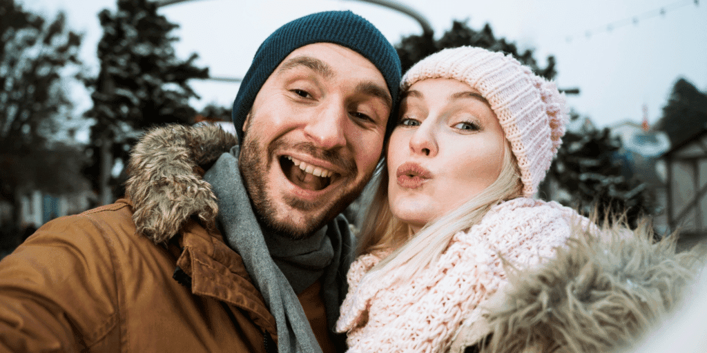 Define what you're looking for. A man and woman in winter jackets, knit hats, and scarves take a selfie while shopping for Christmas trees.