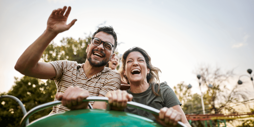 He shouldn't be afraid to have fun. A man in glasses laughs with his girlfriend on an amusement park ride.
