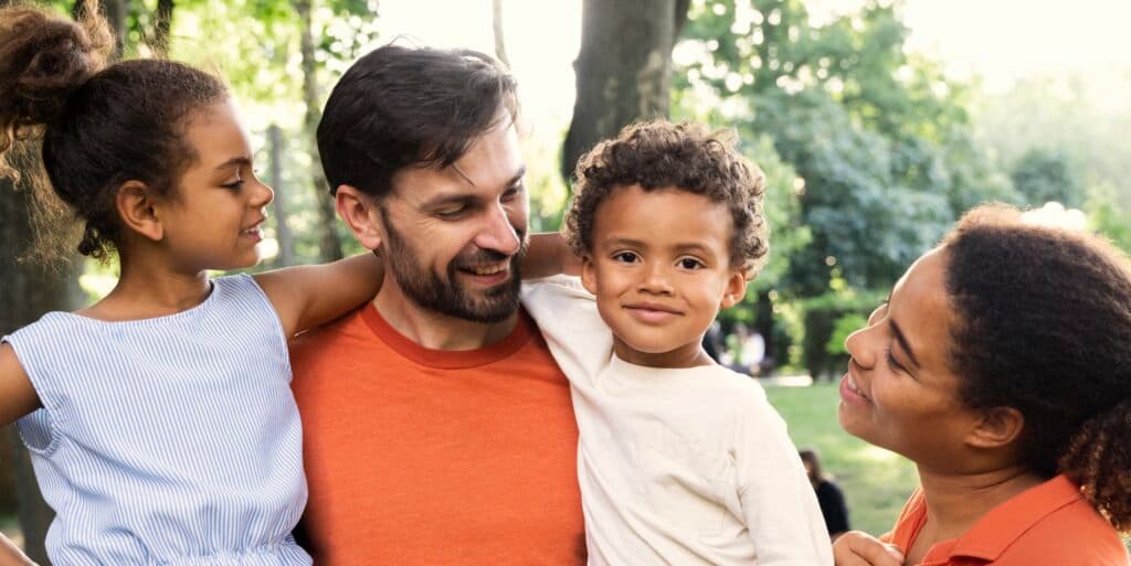 Two adolescent children hug a father while their mother looks at them smiling.